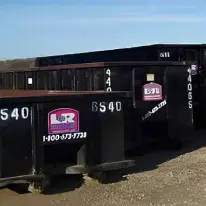 A group of black dumpsters sitting on top of gravel.